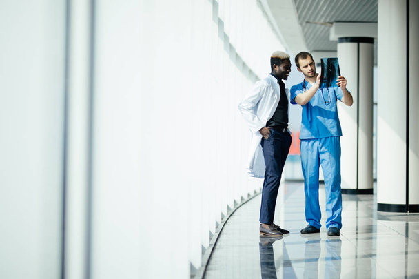 zdravotnictví, lékařské a radiologie koncept - dva Smíšené rasy lékaři při pohledu na rentgen v moderní nemocnici - Fotografie, Obrázek