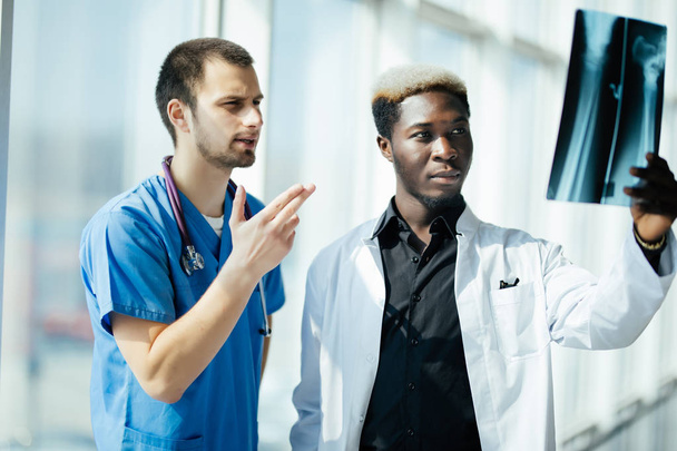 Twee gemengd ras mannelijke artsen onderzoeken x-ray op moderne kantoor van ziekenhuis - Foto, afbeelding