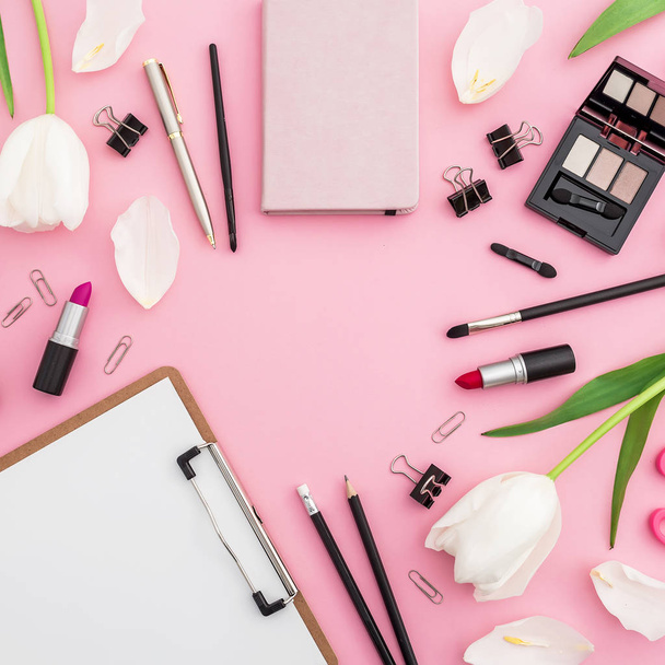 Pohled shora nepořádek na růžové tabulka s kosmetikou, papírnictví a tulipány - Fotografie, Obrázek