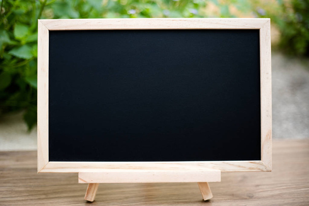 Black board on wood table top with sun and blur green tree bokeh - Foto, imagen
