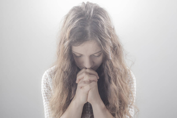 Γυναίκα προσεύχεται σε λευκό φόντο με λάμψη. - Φωτογραφία, εικόνα