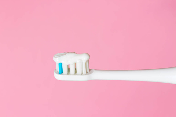 Λευκό ηλεκτρική οδοντόβουρτσα και οδοντόκρεμα σε ροζ φόντο. Η έννοια της καλή στοματική υγιεινή. Κοντινό πλάνο. - Φωτογραφία, εικόνα