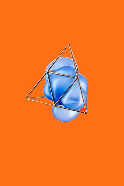 Golden triangular pyramid with a blue turquoise balloon isolated on orange background, Trigonometric representation of a volume - Photo, Image