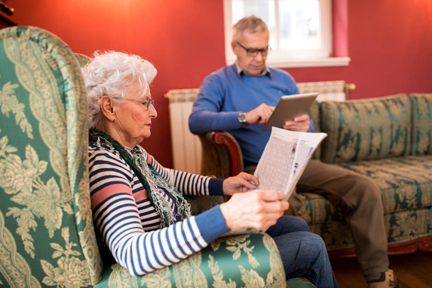 Senior lovely couple relax at home while reading newspaper and using tablet - Foto, immagini