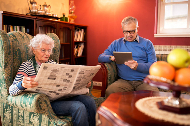 Senior couple relax at home while reading newspaper and using tablet - Foto, Imagem