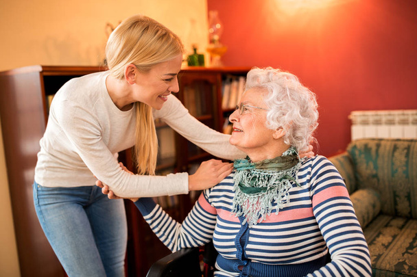Sonriente nieta positiva visita a su abuela enferma en casa
 - Foto, Imagen