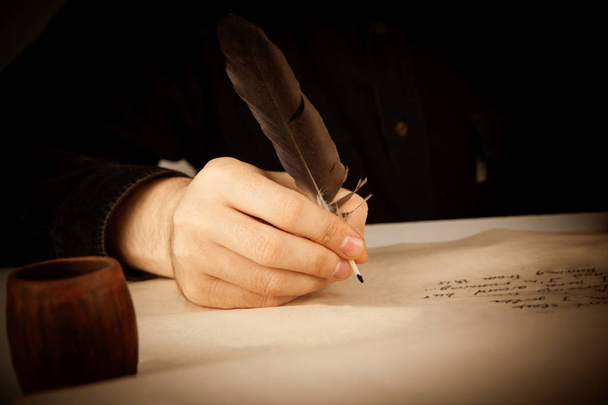 Писатель держит перо над письменной бумагой и пишущей p
 - Фото, изображение