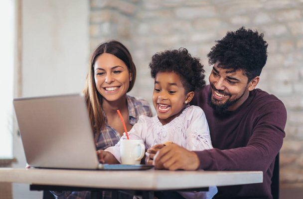 Meisje en gemengd ras ouders laptop thuis gebruiken - Foto, afbeelding