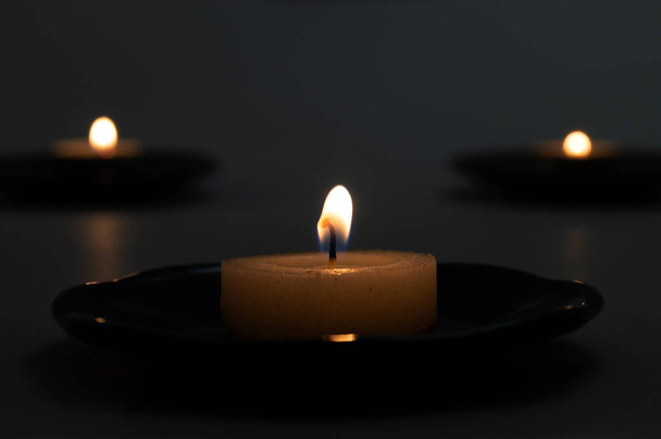 Trois bougies rondes avec mèches brûlantes sur des supports en porcelaine en noir
. - Photo, image