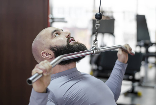 Male athlete doing exercises on pulldown machine in the gym, healthy lifestyle - Foto, imagen