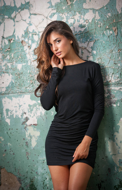 young lady with short black mulled skirt and long hair posing against a wall - Foto, immagini