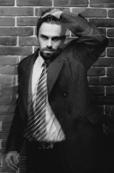 Divatos jól öltözött férfi szakáll jelentő szabadban keres el portréja, magabiztos és koncentrált érett férfi kabát állva egy tégla fal háttér, elegáns divat modell. - Fotó, kép