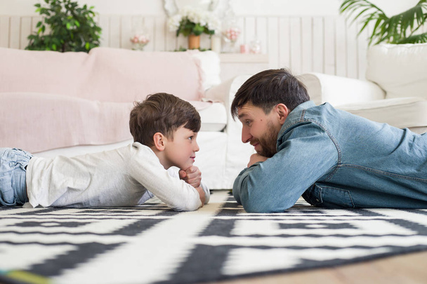 Father's care and protection remain as a pillar of strength throughout children's lives! Side view portrait of adult parent and his child lying on the floor and playing 'who blinks first' game. - Fotoğraf, Görsel