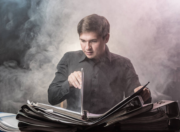 Young man emotionally sitting in front of documents in the smoke - Photo, image