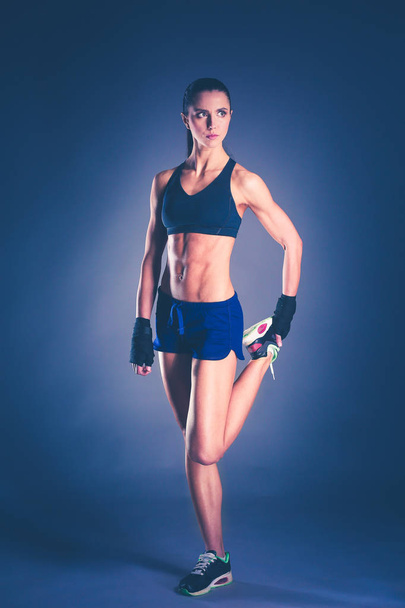 Muscular young woman posing in sportswear against black background. - Zdjęcie, obraz