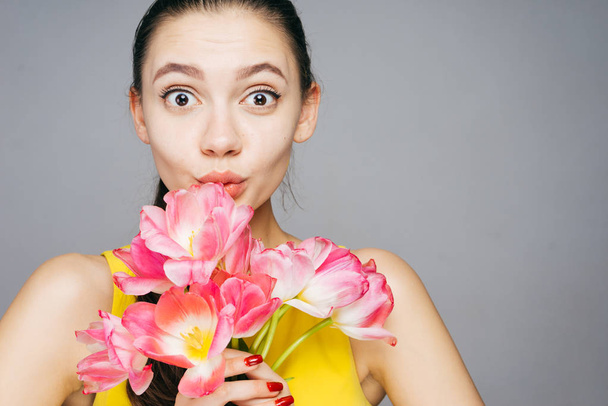 cute funny girl in a yellow dress holding a bouquet of fragrant pink flowers, looks surprised - Photo, Image