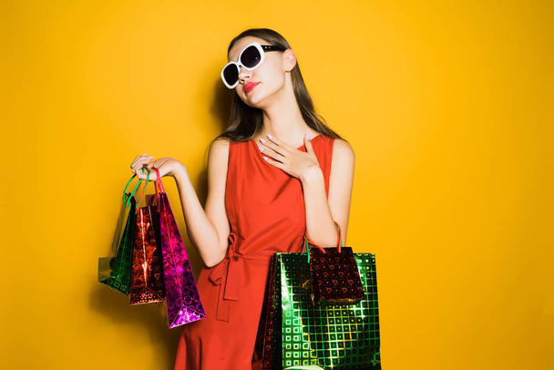 a young beautiful girl in a red dress and sunglasses, went shopping on a black Friday - Foto, imagen