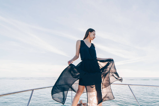 an attractive young girl in a black dress is standing on her white yacht, sailing to the Caribbean islands - Valokuva, kuva