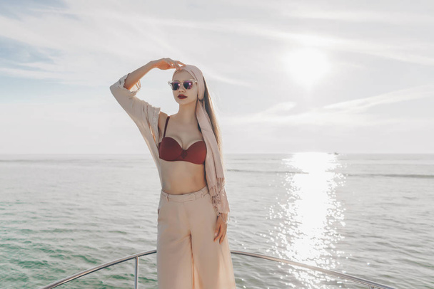 a luxurious young woman in sunglasses and with a headscarf on her head travels the Caribbean sea on her white yacht, enjoys a rich life - Foto, imagen