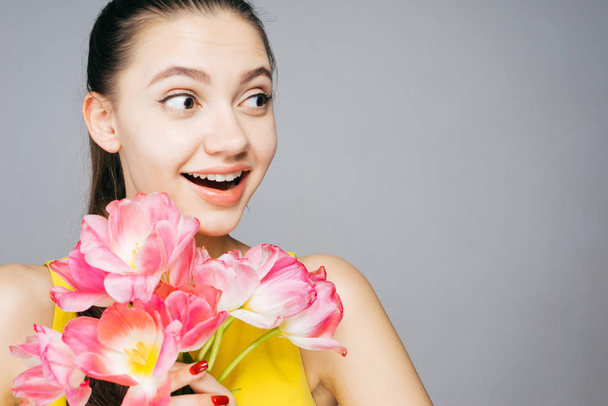 surprised happy girl in yellow dress holds a big bouquet of fragrant pink flowers, enjoys spring - 写真・画像