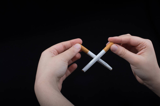Рука держит скрещенные сигареты на черном фоне - Фото, изображение