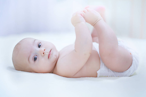 Funny little baby boy wearing a diaper playing on a white blanke - Foto, imagen