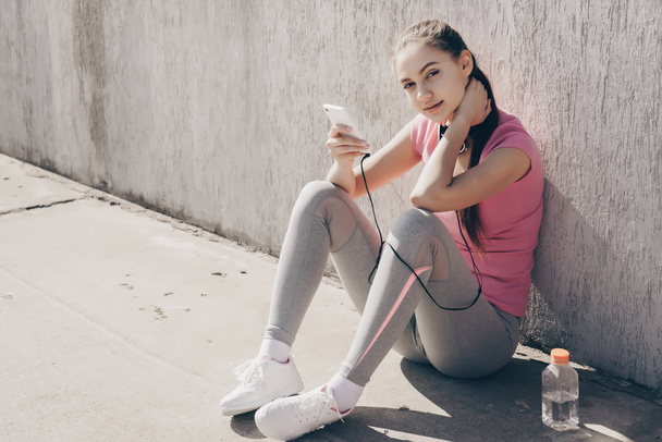 A young girl rests after a zealous street workout, drinks water and gets strength - Фото, изображение