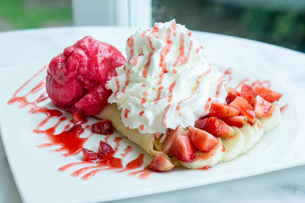 десерт из клубники с мороженым на столе из белого дерева в кафе
 - Фото, изображение