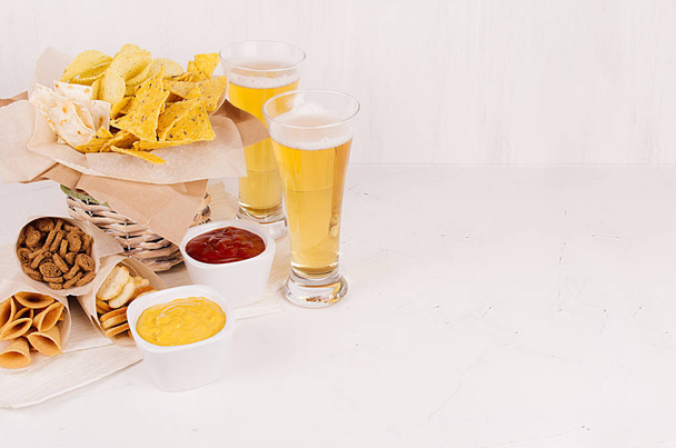 Summer fast food - different crunchy snacks and red, yellow sauce in white bowls, cold beer on soft white wood board, copy space.  - Photo, Image