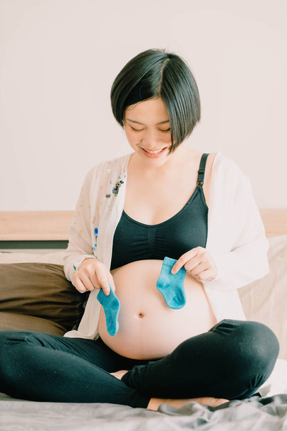 Young beautiful Asian pregnant woman lying in bed and choosing b - Foto, immagini