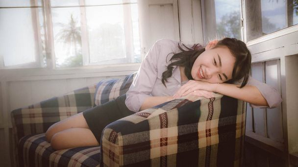 アジアの女の子の笑顔と夜明けヴィンテージスタイルの窓からの光でソファーで横になっているソファーでやま - 写真・画像