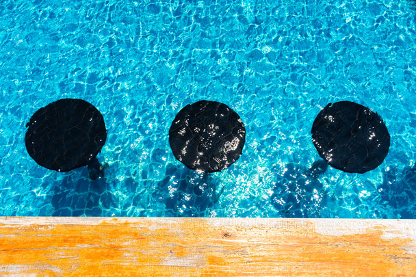 Cadeira marrom na piscina com reflexão rasgada azul, assento de madeira na piscina, mesa de madeira ao lado da piscina
 - Foto, Imagem