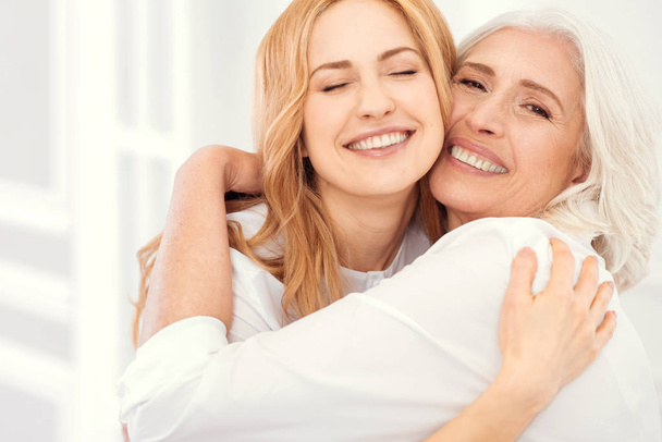 Radiant mother and daughter beaming into camera while hugging - Foto, immagini