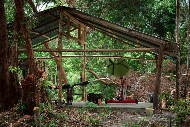 Ερασιτεχνικό ξύλινο υπαίθριο γυμναστήριο στη μέση της ζούγκλας με ποδήλατο γυμναστικής, τύπου πάγκου και χαζός καμπάνες. Καμπότζη, Κοχ Ρονγκ Σανλοεμ νησί.  - Φωτογραφία, εικόνα