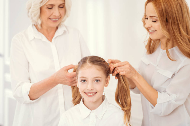 Loving granny and mother combing hair of charming granddaughter - Foto, immagini