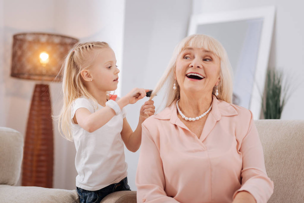 Positive blonde girl brushing her grandmothers hair - Valokuva, kuva