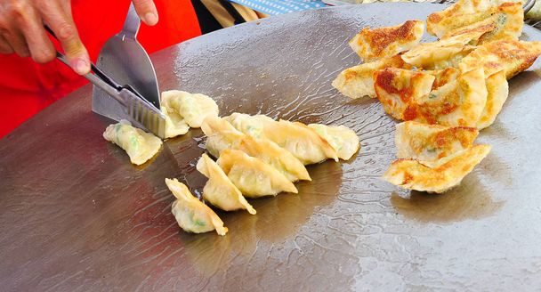 Een straat verkoper die verse Gyoza (Japanse gebakken dumplings) op een enorme stalen pan bedekt met warme kookolie voor het passeren van klanten - Foto, afbeelding
