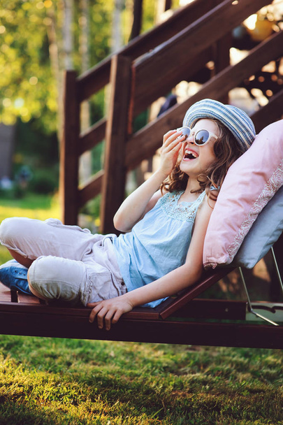 summer portrait of happy kid girl relaxing on lounger in garden on vacation - Fotó, kép