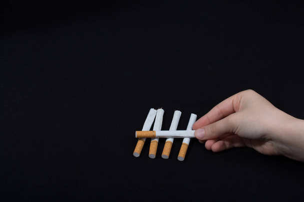 Hand houdt gekruiste sigaretten op zwarte achtergrond - Foto, afbeelding