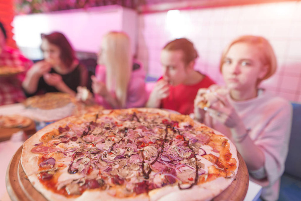 Смачна велика піца в піцерії, на тлі групи молодих людей. Студенти їдять піцу в затишному ресторані
 - Фото, зображення