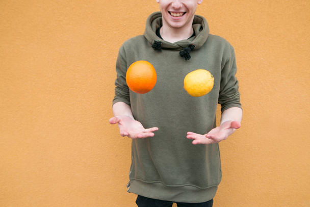 Pozitivní mladý muž žongluje s citronu a pomeranče na pozadí oranžové zdi. Koncept ovoce - Fotografie, Obrázek