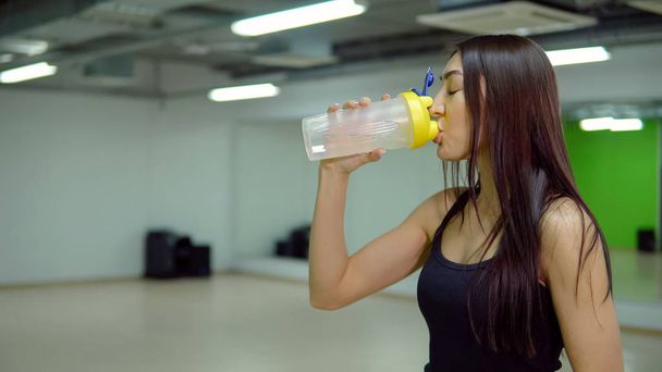 Молода жінка в спортивній формі п'є воду в спортзалі
 - Фото, зображення