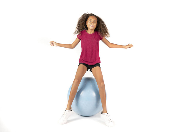 Jovem criança brincalhão ou pré-adolescente menina birracial com cabelo encaracolado marrom jogando ou se exercitando em uma grande bola de borracha
 - Foto, Imagem