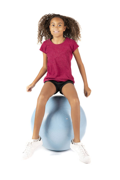 Jeune enfant ludique ou fille pré-adolescente biraciale aux cheveux bruns bouclés jouant ou faisant de l'exercice sur une grosse boule en caoutchouc
 - Photo, image
