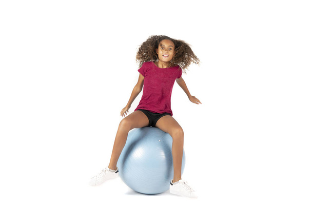 Молодой игривый ребенок или доподростковая девочка с каштановыми кудрявыми волосами играет или тренируется на большом резиновом мяче
 - Фото, изображение