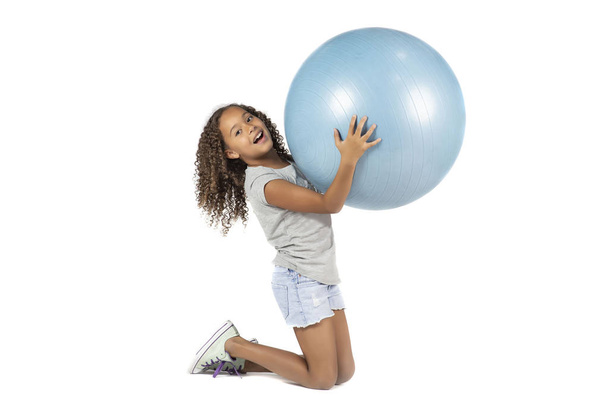 Małe dziecko figlarny lub Pre teen dziewczyna biracial o brązowych włosach kręconych zabaw czy ćwiczeń na dużą gumową piłkę - Zdjęcie, obraz