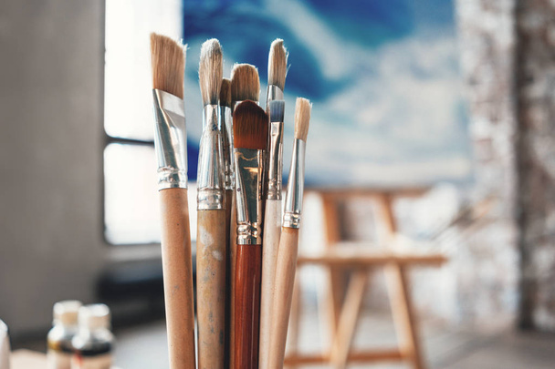 Artist paintbrushes closeup on blurred background of painter workshop. Different brushes in drawing studio interior. Creative concept - Photo, Image