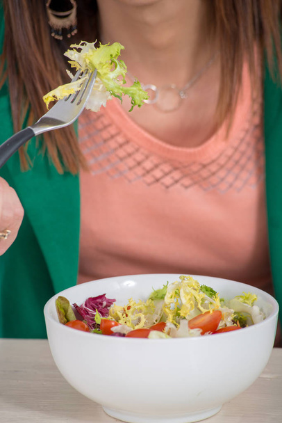 brunette vrouw met groene jas, eten Salade  - Foto, afbeelding