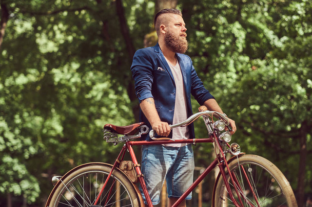 Man gekleed in casual kleding, wandelen met een retro fiets in een park. - Foto, afbeelding
