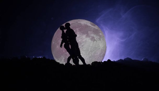 Silhouette of couple kissing under full moon. Guy kiss girl hand on full moon silhouette background. Valentine`s day decor concept. Silhouette of loving couple kissing against the moon - Photo, Image